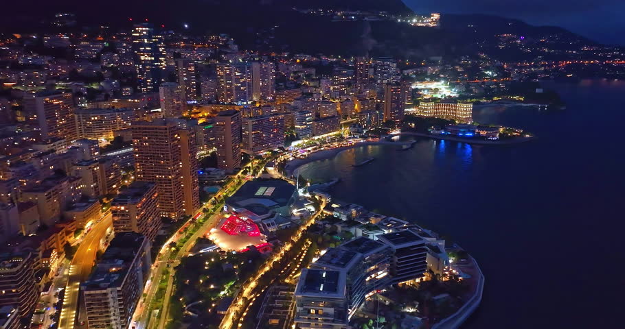 Aerial establishing shot of illuminated city buildings. Aerial view of illuminated skyscraper in residential city at night, Monte Carlo, Monaco
