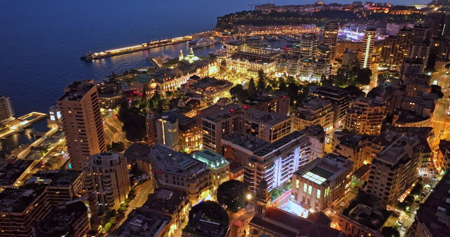 Aerial establishing shot of illuminated city buildings. Aerial view of illuminated skyscraper in residential city at night, Monte Carlo, Monaco