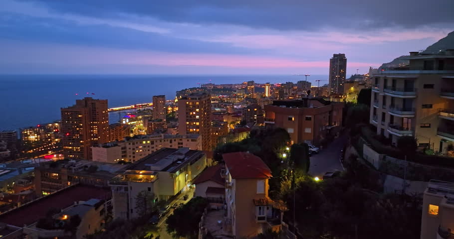 Aerial establishing shot of illuminated city buildings. Aerial view of illuminated skyscraper in residential city at night, Monte Carlo, Monaco