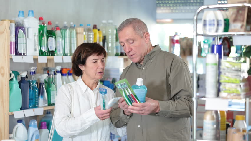 Couple mature man and woman buyers choosing dental care products in household chemicals store 