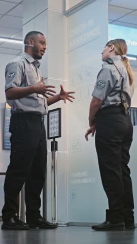 Crowded Airport Terminal: Two Multiethnic Security Officers in Uniform Talking, Standing at Security Checkpoint, Showing Male Passenger the Way to Boarding Gate for His Plane Flight. Vertical Shot.
