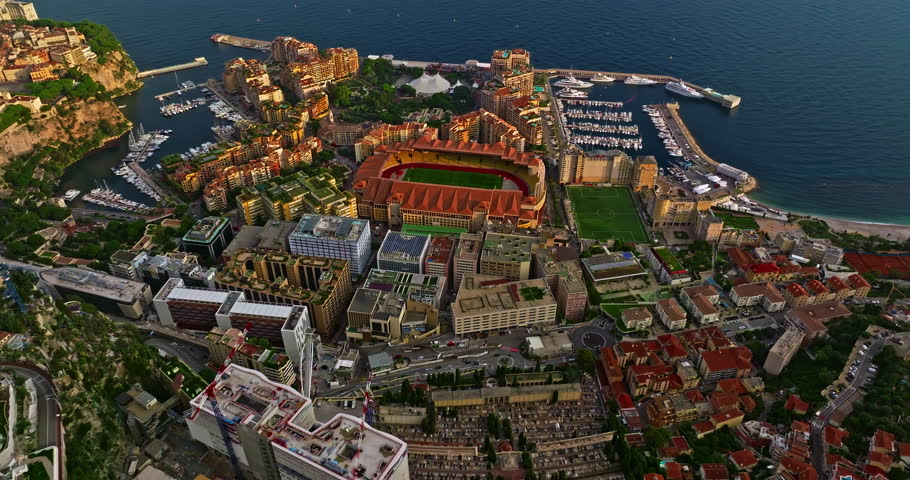 Aerial view of the city center of Monaco. Establishing shot showcases luxury yachts moored in Monaco Bay, the Palais Princier de Monaco, and luxury apartment buildings of Monte Carlo