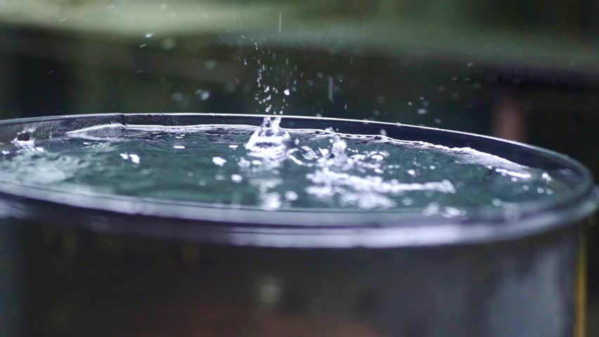 Rain drops falling into barrel, collecting rain, water splashing