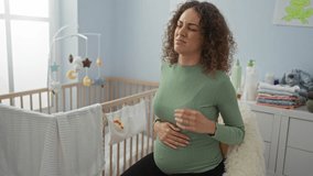 Pregnant woman with curly hair in a bedroom sitting on a chair experiencing neck pain near a cradle under sunlight from a window. - Powered by Shutterstock - Get 15% off with code: PIKWIZARD15