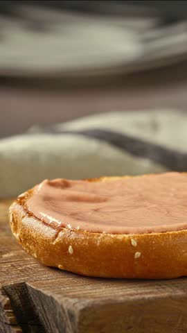 cook put grilled burger meat with melted cheese on bread bun on wooden cutting board, food closeup