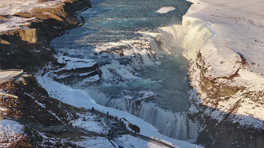 An aerial view of Gullfoss waterfall in Iceland during winter, showcasing the cascading water and the group of tourists observing the natural wonder.