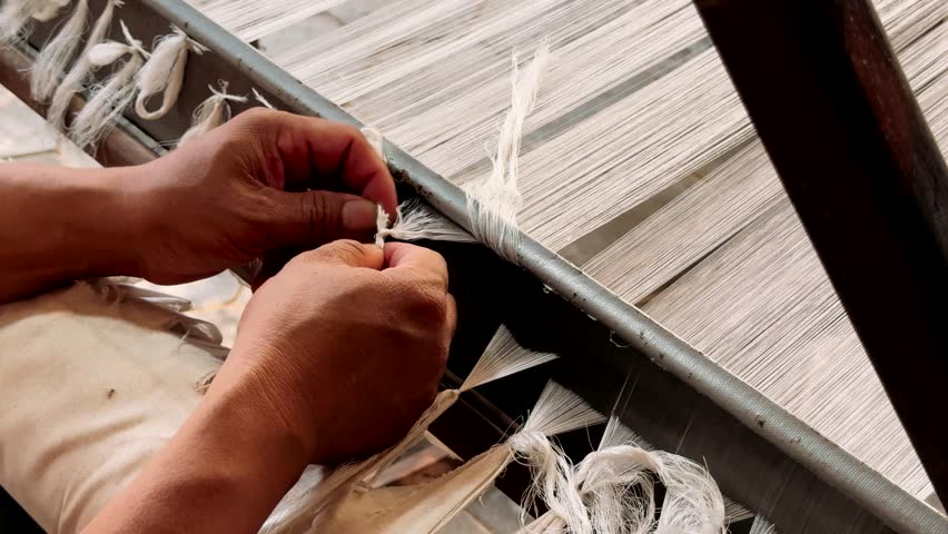 Silk weaving machine in operation. The girl works at the machine creating. Woman weaving on a traditional loom. Hand weaving cotton. Traditional cotton weaving.