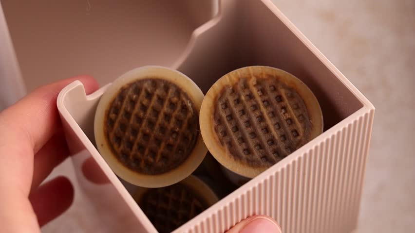A woman's hand shows the compartment for used capsules from a coffee machine. Recyclable plastic coffee capsules with a paper lid