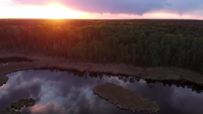 Slow sideways flight over lake at sunset. Stunning sunset over a dense forest with silhouettes of trees