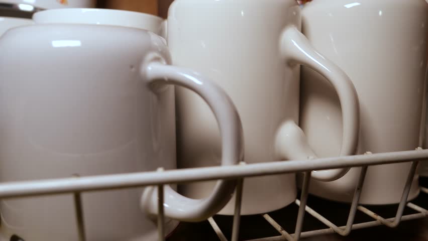 White ceramic coffee mugs drying on metal rack after washing, showcasing kitchen cleanliness and domestic organization in minimalist home setting