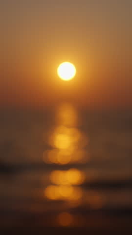 A seascape at golden hour captured in soft focus, where gentle waves ripple beneath the softened light and bokeh circles form on the seawater due to the sunset
