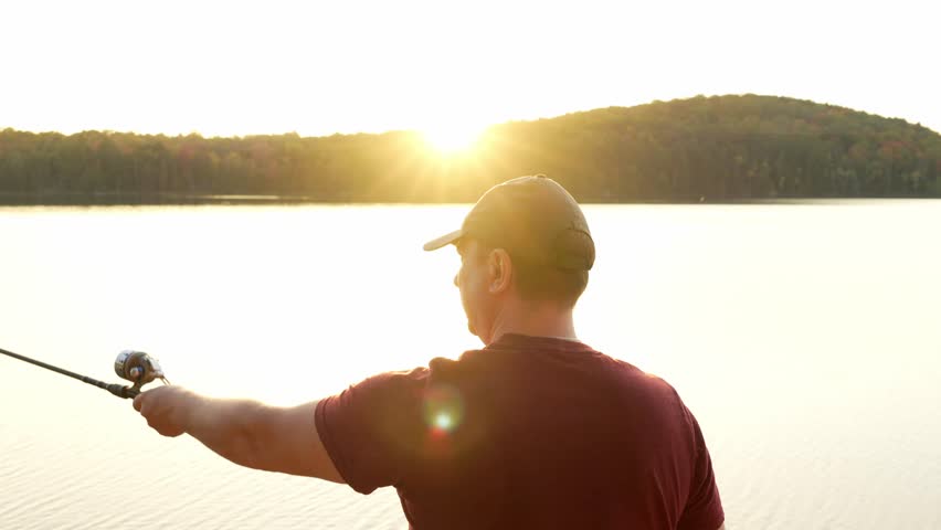 Man Fishing on the lake, Pulls a Reel of Fishing Line at Sunset in Summer, Close-up. Fisherman Catches a Fish. Fisherman With Spinning Rod in His Hand.