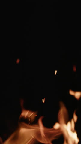 A close-up view of a fire showcases bright orange sparks and flames against a dark backdrop, emphasizing the dynamic movement and rich texture of combustion