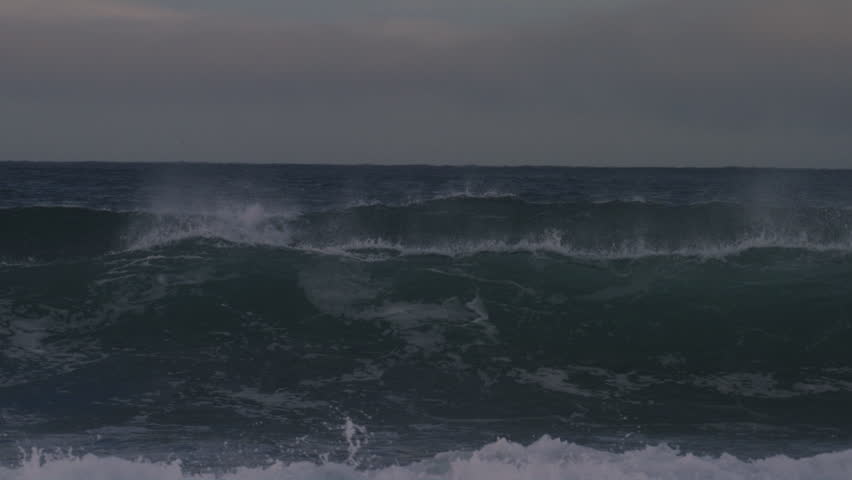 Arctic waves crash in slow motion as surfer pops up and carves under stormy sky with snow on mountains