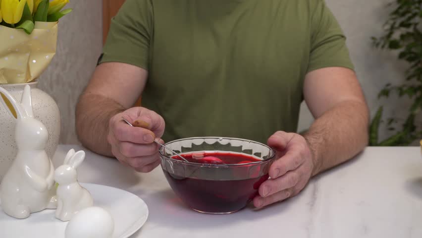 4k. Coloring chicken eggs in the traditional red color for Easter. hands dip a spoon with eggs in a coloring solution.