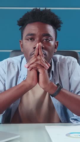 Young man contemplates thoughtfully with fingers interlocked, showing a mix of determination and introspection. The atmosphere around him radiates the essence of urban life in Africa.