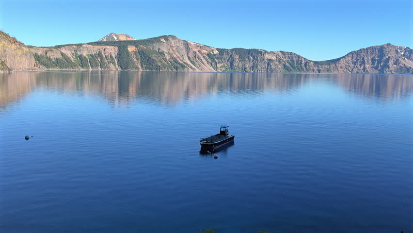 A boat floating on the calm waters of Crater Lake, Oregon with towering cliffs in the background