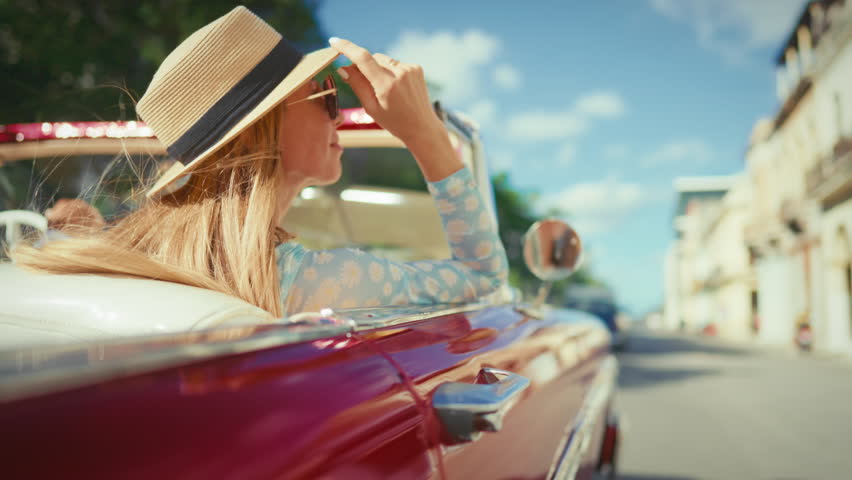 Woman passenger inside retro red cabriolet, car trip in summertime, back view. Luxury life and freedom, rich lady enjoying tourist journey in vintage auto, beautiful sunny summer day, be happy