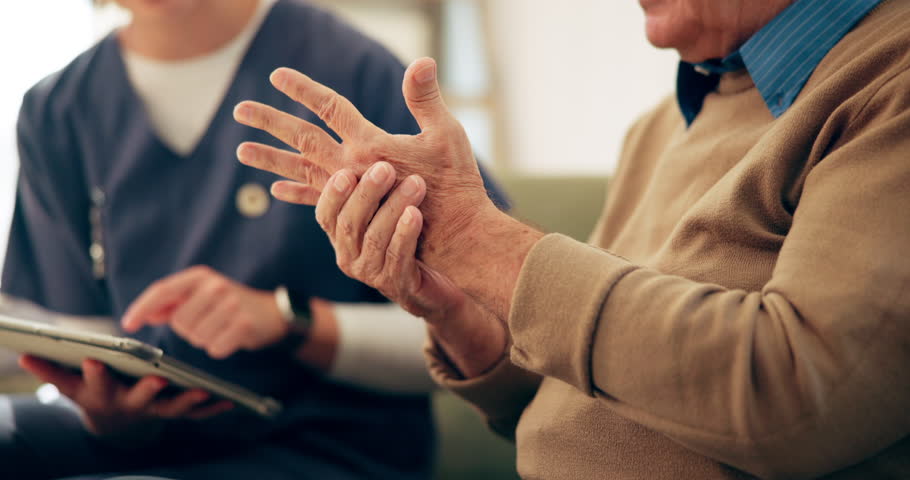 Caregiver, hand and senior person with arthritis, nursing home and numbness of fingers in lounge or pain. Retirement, closeup and pensioner with carpal tunnel syndrome, helping and nurse with tablet