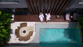 Couple relax by pool in hotel or villa. Family of man and woman in resort chill at the private terrace wearing white robes on their honeymoon vacation. - Powered by Shutterstock - Get 15% off with code: PIKWIZARD15