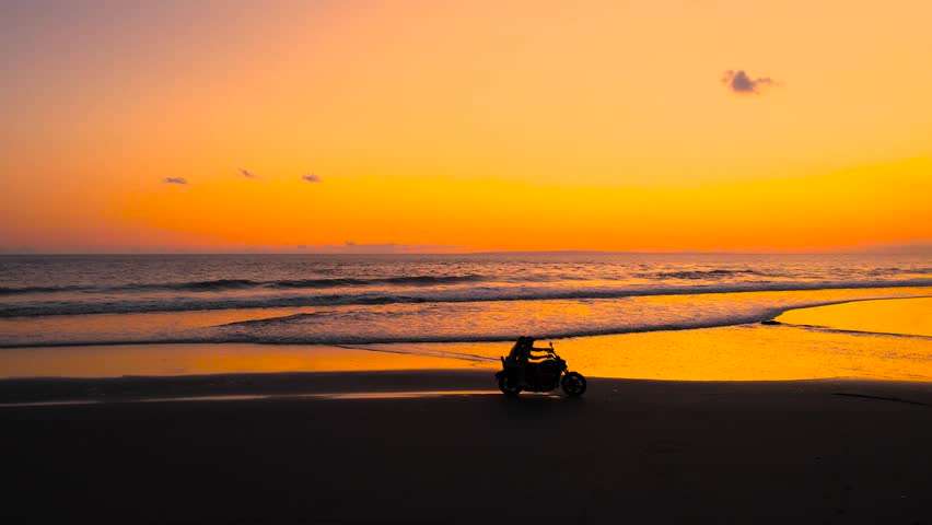 Couple riding a motorbike along the beach in Bali at sunset, with golden light reflecting on the ocean waves, feeling freedom and vacation vibe, independence. Motorcycle driving, moto trip