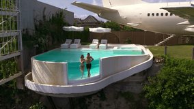 Couple relaxing in infinity pool on their luxury exotic hotel made from airplane. Aircraft repurposed for private villa in Bali. VIP vacation in luxurious setting of unique design.  - Powered by Shutterstock - Get 15% off with code: PIKWIZARD15