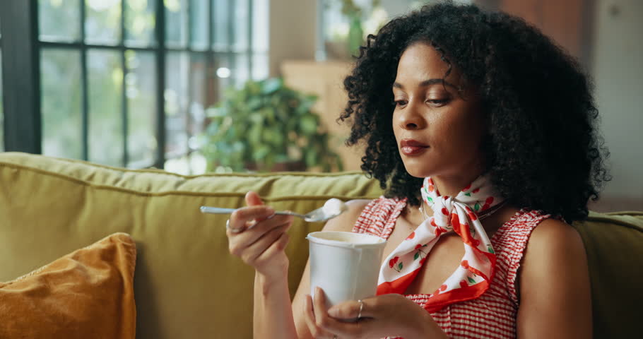Woman, ice cream and happy on sofa with snack for satisfaction, eating and craving in house. African girl, gelato and smile in home living room on couch for frozen dessert or yogurt and sweets