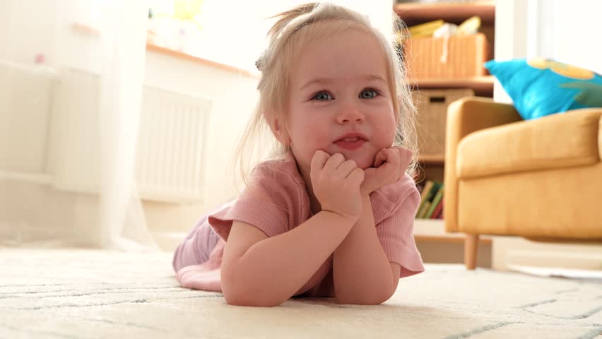 Cute little child girl 3 years old is sitting at home on the carpet in the children's room
