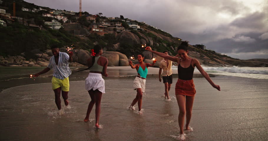 Beach, dancing and friends with vacation, sparklers and celebration with tropical island. Happy people, seaside or group with party, fireworks or summer holiday with social event, freedom or Zanzibar