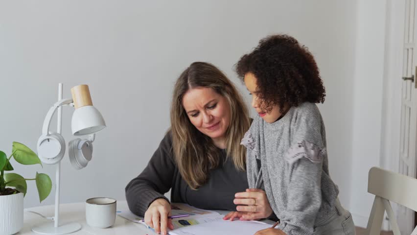 Caucasian mother and African American daughter studying at home, doing homework in cosy white room. Parent teach, child school girl learn knowledge, write exercise read book. Education for children
