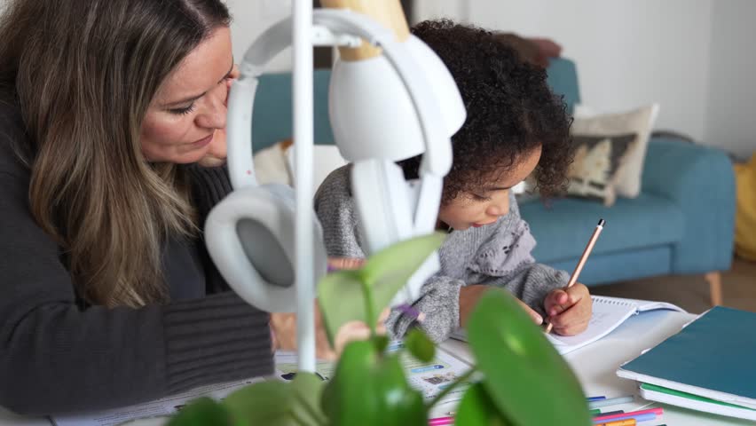 Caucasian mother and African American daughter studying at home, doing homework in cosy white room. Parent teach, child school girl learn knowledge, write exercise read book. Education for children