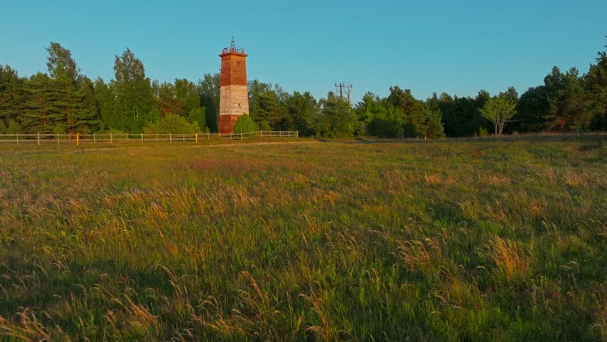 Flying towards a soviet style old lighthouse over some fields and country road