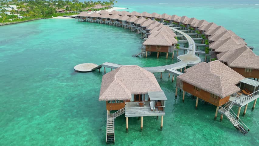 Maldives Island with tropical palm trees and luxury hotel resort apartments. Sunny day with Crystal clear ocean water and sandy beach. Aerial flyover shot.