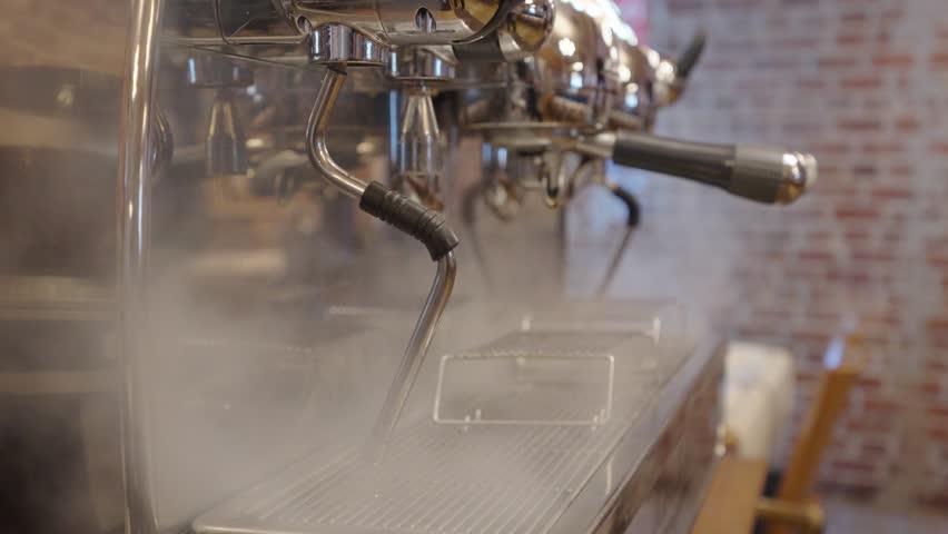Close-up of a professional espresso machine steaming in a café setting, with visible mist and metallic surfaces, creating a cozy barista atmosphere.
