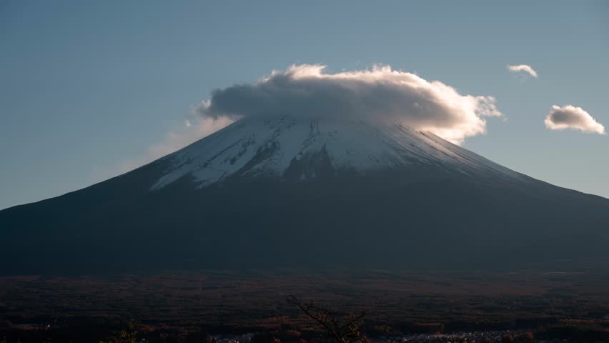 Lenticular cloud hovering over snow capped mount fuji, dramatically transforming during golden sunset light across japanese volcanic landscape