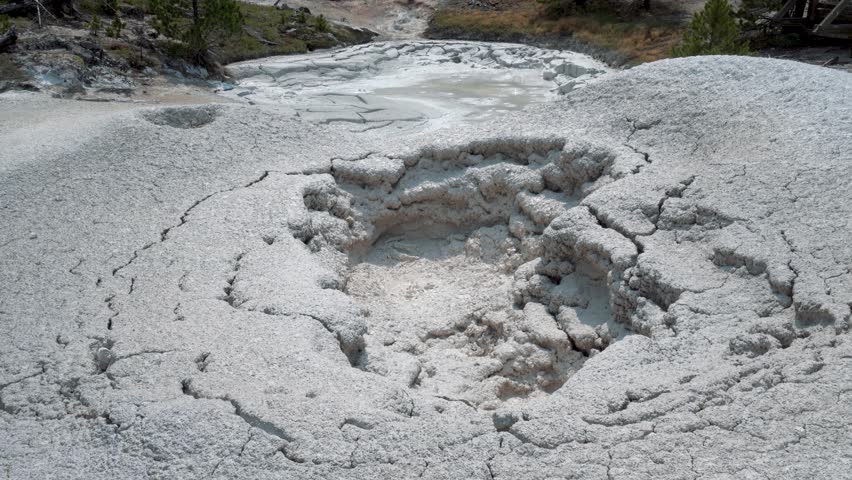 Bubbling mud pot in Yellowstone, releasing thick steam as mineral rich mud boils in a geothermal area, tilt up across textured cracks and patterns