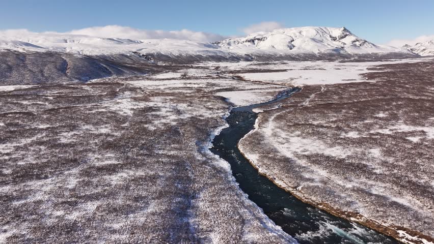 Wide aerial view of Brúarfoss waterfall, Iceland, nestled in a snowy winter landscape with mountains in the background.