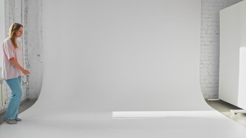 Woman is walking in wide step from the left to the right moving legs and arms filmed on white background. Young adult Caucasian lady in casual clothes is moving in a hurry. Theme of human body motion.