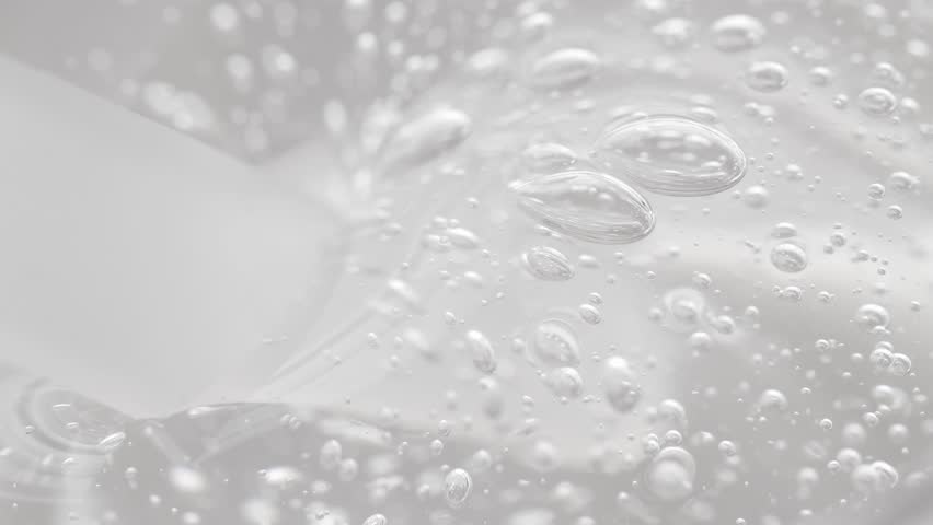 Transparent gel texture with bubbles is mixed with a cosmetic spatula, macro.