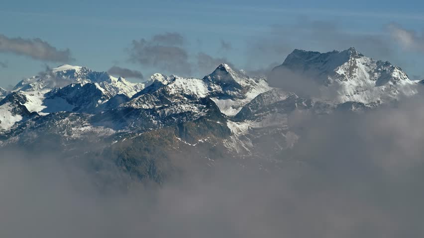 Cinematic aerial shot of snow capped mountain peaks with clouds in front