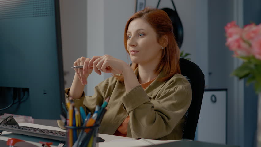 In a cozy home office, a woman engages in a virtual meeting while diligently taking notes in her notebook, showcasing remote work productivity.