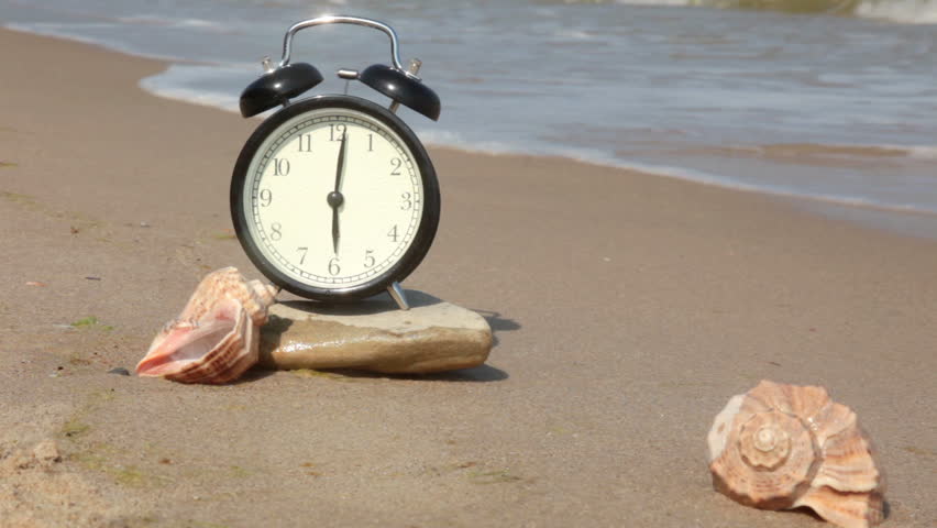 Beach. Clean soft sand. Surf. On the stone is an alarm clock. Next to them are