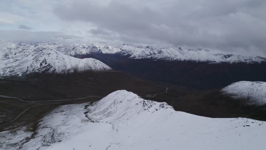 Stunning drone flight over snowy mountains of Alaska during cloudy day. Hatchers Pass in the valley between white covered peaks. Wide shot
