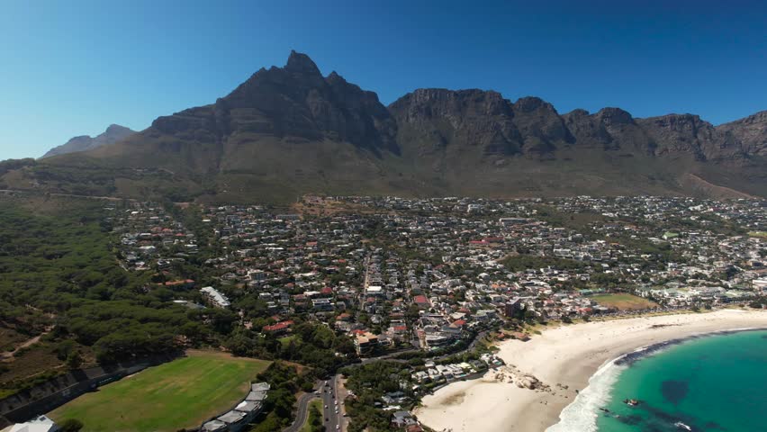 Beautiful landscape with sandy beach, blue bay water and mountain range in Cape Town. Noble district with housing area and villas in South Africa. Drone wide shot.