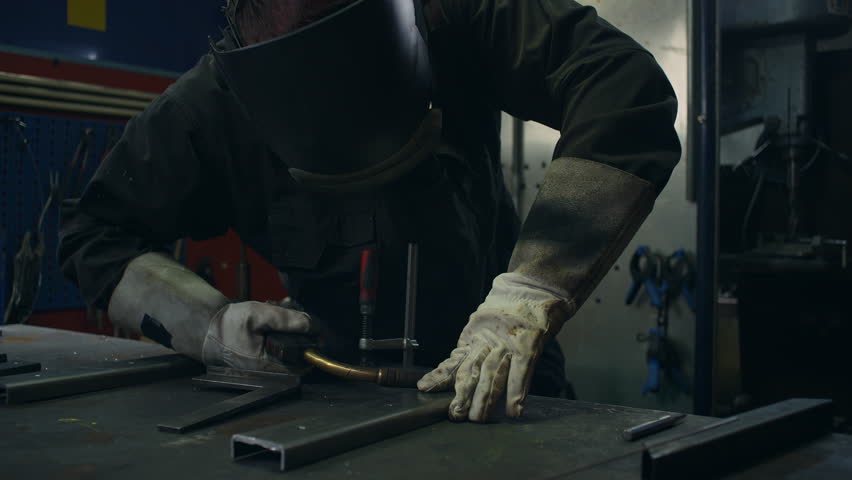 Skilled welder worker with experience in metal fabrication, using MIG welding techniques to create sparks and shape metal components, close up shot.