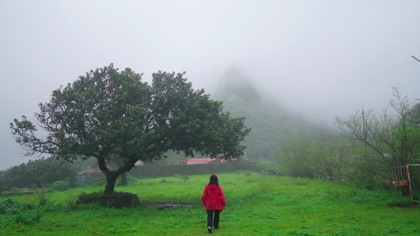 Girl hiking outdoors in fog on a rainy day near Shivkhind pass in Lonnavala, Maharashtra, India. Tourist exploring Sahyadri hills during monsoon season. Travel and holidays concept