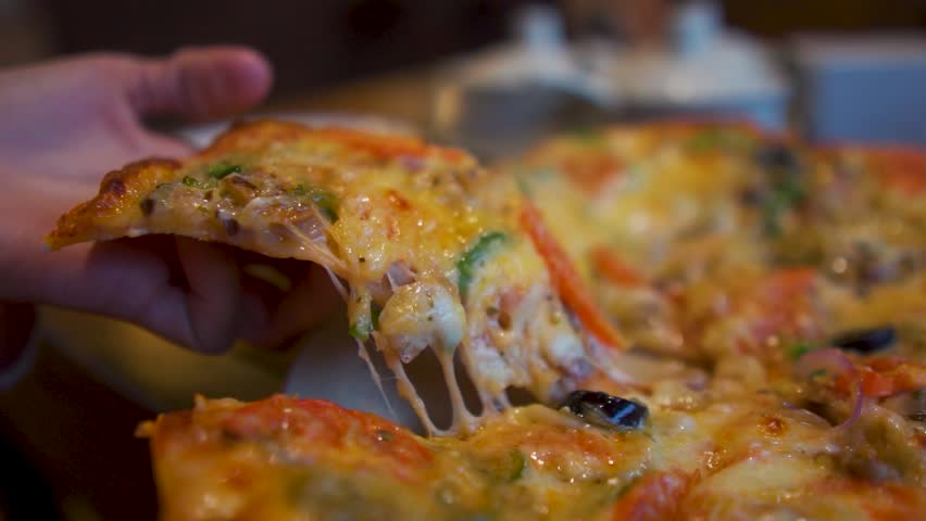 Close up shot of girl lift Pizza slice in restaurant. Woman hand eating Italian pizza. Close-up of fresh Cheese Pizza. Cheese stretching as a slice is pulled away.