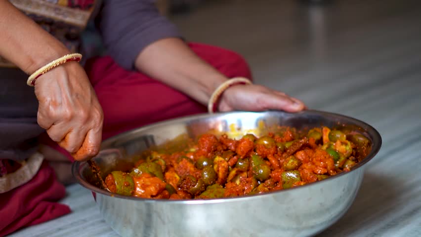 Close up shot of Indian woman making traditional mango pickle at home. Indian woman wearing bangles in hands and mixing spices in pickle. Female preparing food in kitchen. An Indian housewife.