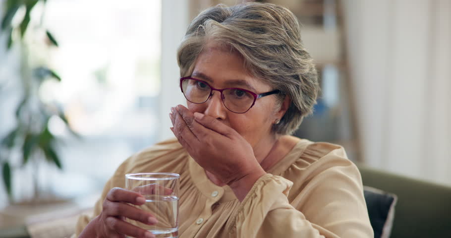 Senior woman, drinking water and pills on sofa in home with morning routine, schedule and health in retirement. Elderly person, glass and liquid for medicine, supplement and benefits for wellness