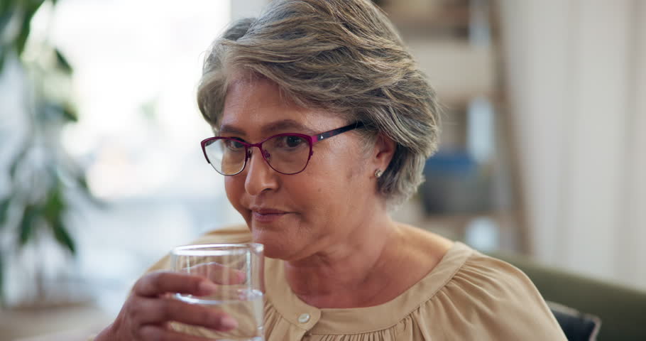Senior woman, drinking water and pills on sofa in home with morning routine, schedule and health in retirement. Elderly person, glass and liquid for medicine, supplement and benefits for wellness